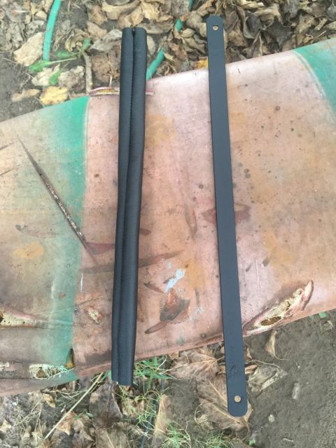 1993 Ford Bronco - Two black rubber hoses and a metal bracket are shown on a rusty surface, possibly for a vehicle repair or restoration project.