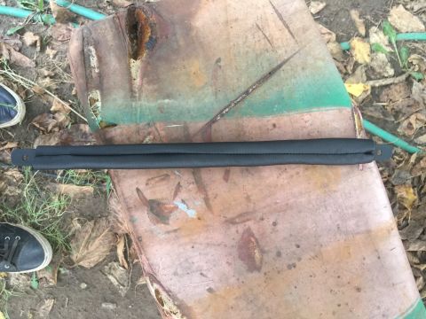 1993 Ford Bronco - A black padded trim piece is shown resting on a rusty metal surface outdoors.