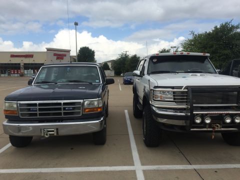 1993 Ford Bronco - Two Ford trucks are parked in a parking lot in front of a Mattress Firm store. The truck on the left is dark blue, and the truck on the rig…