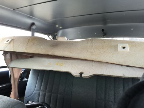 1993 Ford Bronco - The interior of a vehicle shows two stacked, disassembled headliner panels resting on dark gray seats. The panels are beige and appear to b…