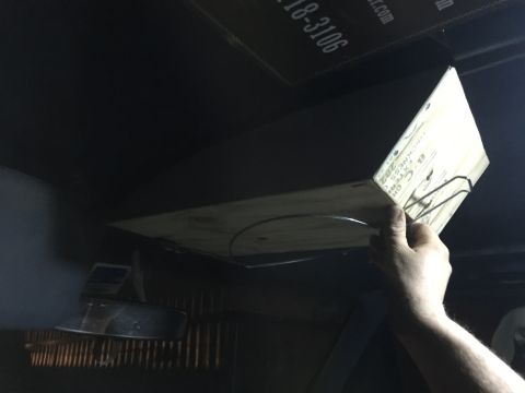 1993 Ford Bronco - A hand holds a piece of plywood with text and a metal clip attached, angled downwards. A dark ceiling with text is visible above, and a met…