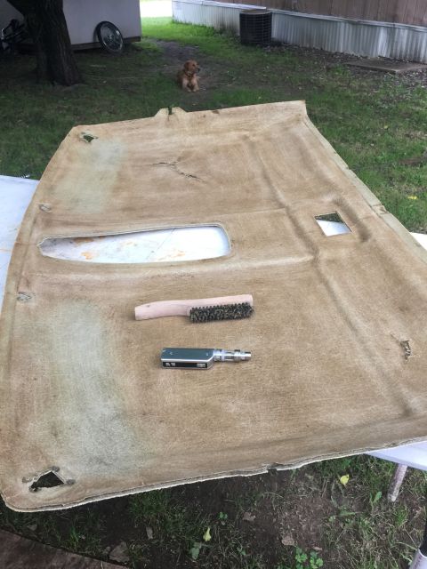 1993 Ford Bronco - A dirty, tan-colored headliner is laid out on the ground. A brush and a vape pen are placed on top of the headliner.