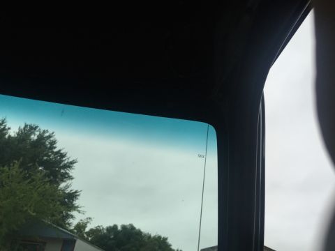 1993 Ford Bronco - View through the windshield of a 1993 Ford Bronco, showing the top portion of the glass with a blue tint and a faint inscription. Trees and…