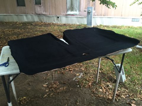 1993 Ford Bronco - A black headliner is laid out on a folding table outdoors, with a pair of blue scissors on the left side of the table.