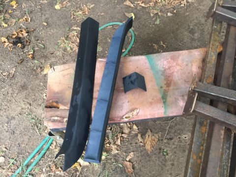 1993 Ford Bronco - Three black plastic trim pieces are laid out on a rusty metal sheet. A green hose is visible to the left of the trim pieces.