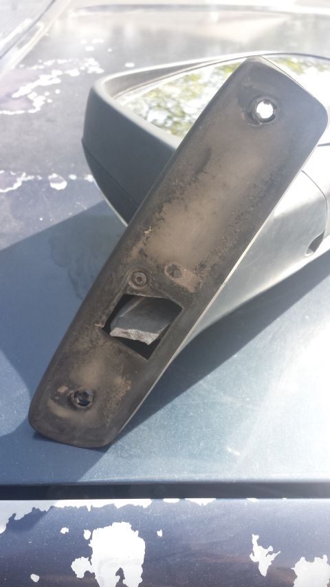 1993 Ford Bronco - A close-up, angled view of a dirty, black plastic trim piece from a side mirror assembly, likely for a 1993 Ford Bronco, is shown resting o…