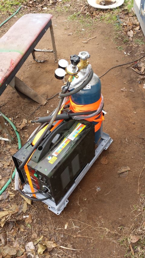 1993 Ford Bronco - A welding machine and a gas cylinder are strapped to a grey metal base. The equipment is situated outdoors on the ground amidst dry leaves…