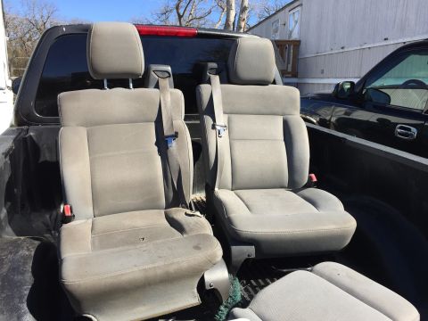 1993 Ford Bronco - Two grey fabric bucket seats with headrests and seatbelts are loaded in the bed of a black pickup truck. A black pickup truck is parked nex…