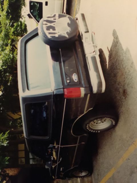 1993 Ford Bronco - A black Ford Bronco is parked on asphalt with a yellow line. A spare tire cover with "TEXAS" and the outline of the state is visible on the…