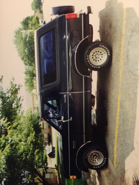 1993 Ford Bronco - A dark blue 1993 Ford Bronco is parked on the side of the road next to a yellow line. The vehicle has a spare tire mounted on the rear and…