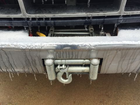 1993 Ford Bronco - The front bumper of a vehicle is covered in ice and icicles, with a winch and tow hook visible. Snow is also present on the upper part of t…