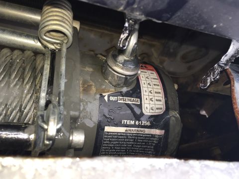 1993 Ford Bronco - Close-up of a winch with a "ITEM 61256" label and a load chart. The winch and surrounding components are wet, with ice visible.