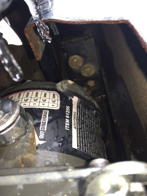 1993 Ford Bronco - A close-up, wet view of a winch with a label that reads "ITEM 61256" and "OUT/DISENGAGE". The winch is mounted to a vehicle frame with visi…