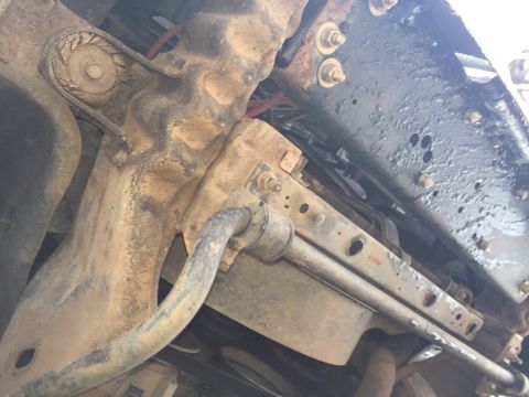 1993 Ford Bronco - The underside of a vehicle shows heavily rusted suspension components, including a sway bar and mounting brackets, attached to a black pain…