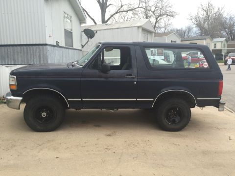1993 Ford Bronco - The side profile of a dark blue Ford Bronco is shown parked on a concrete surface. The vehicle has a two-door body style and appears to be…