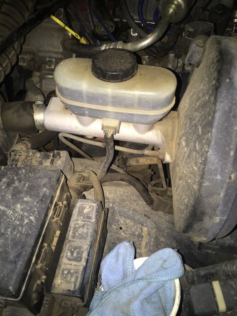 1993 Ford Bronco - The engine bay of a 1993 Ford Bronco shows a dusty brake fluid reservoir and master cylinder assembly, along with fuse boxes and various ho…