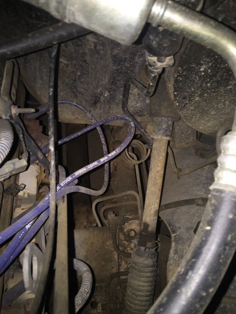 1993 Ford Bronco - A close-up view of engine components in a 1993 Ford Bronco, showing various hoses, wires, and metal parts covered in dirt and grime.