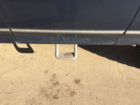 1993 Ford Bronco - A close-up side view of a dark blue vehicle's lower body panel and a silver step-assist mounted below the door. The step has a textured sur…