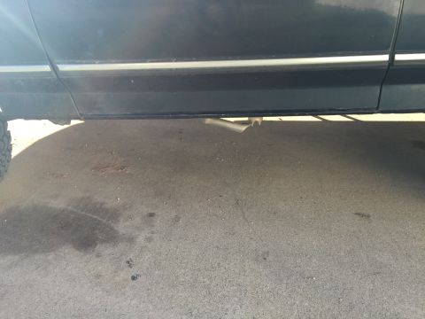 1993 Ford Bronco - The lower side panel and exhaust pipe of a dark-colored vehicle are visible, resting on a concrete surface with some stains.