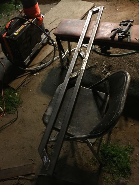 1993 Ford Bronco - Two long, angular metal pieces that appear to be part of a custom fabrication project are resting on a black chair. A welding machine is vi…