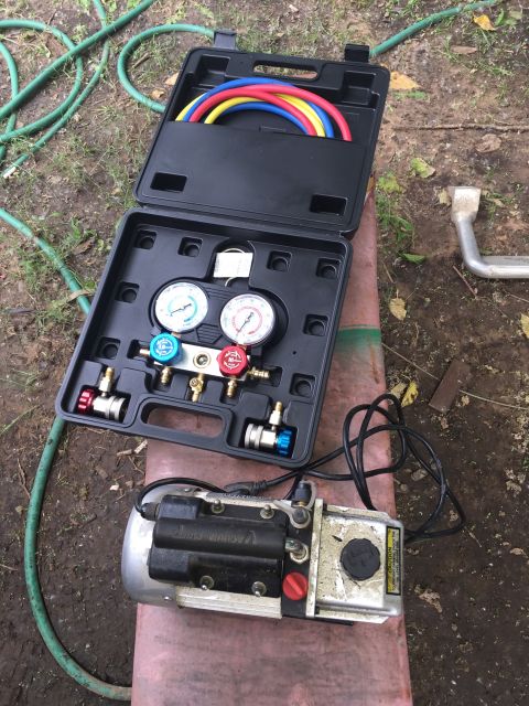 1993 Ford Bronco - A set of AC manifold gauges and a vacuum pump are laid out on the ground next to a green hose.