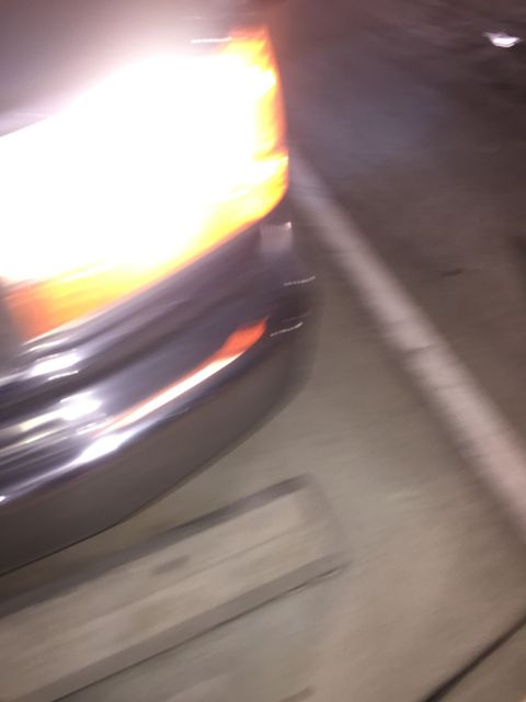 1993 Ford Bronco - A close-up, motion-blurred shot of the front corner of a vehicle at night, showing the illuminated headlight and chrome bumper.