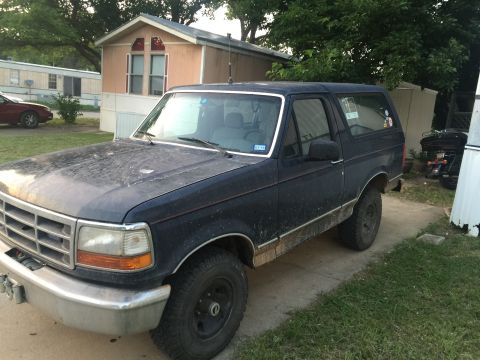 1993 Ford Bronco - A dark blue, two-door Ford Bronco is parked on a concrete driveway in front of a mobile home. The vehicle appears dusty and shows some wear…