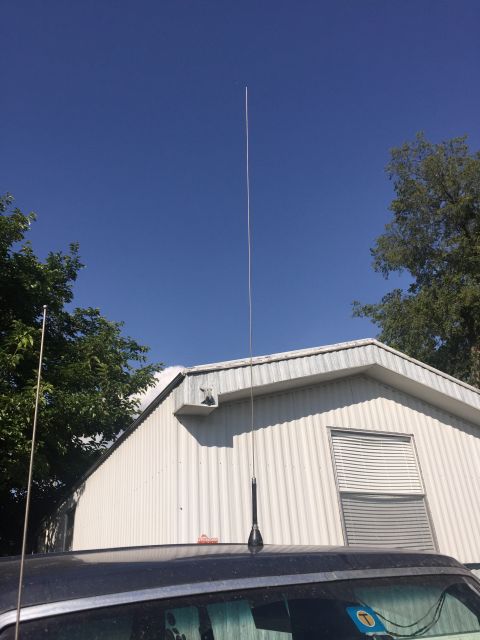 1993 Ford Bronco - A tall, thin antenna extends vertically from the roof of a dark-colored vehicle, positioned in front of a white, corrugated metal building…