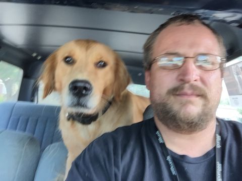 1993 Ford Bronco - A man and a golden retriever dog are in the front seats of a vehicle. The man is wearing glasses and a dark t-shirt, and the dog is wearing…