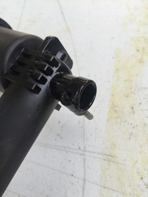 1993 Ford Bronco - A close-up, angled view of a black plastic component, possibly a pump housing, with a ribbed section and a cylindrical outlet. The part is…