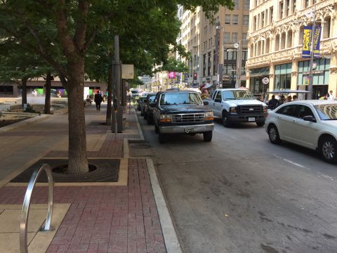 1993 Ford Bronco - A black Ford Bronco is parked on the street next to a sidewalk with trees. The vehicle is viewed from the front-left angle.