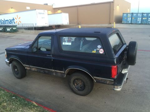 1993 Ford Bronco - The rear passenger side of a dark blue 1993 Ford Bronco is shown parked on asphalt next to a curb. A spare tire is mounted on the rear door…