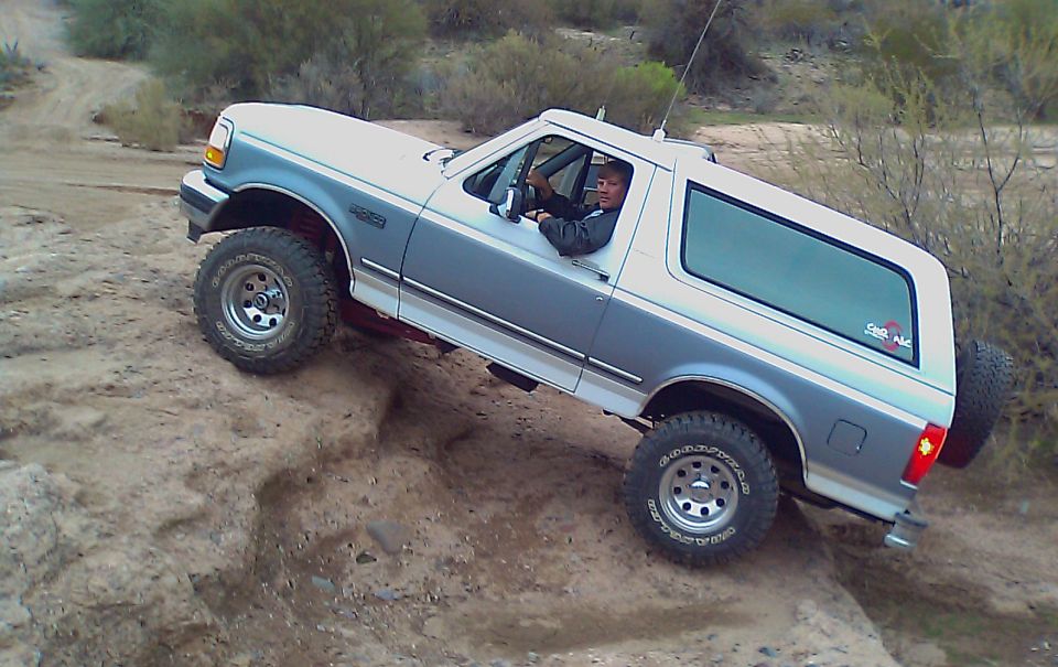 White and grey Ford Bronco driving off-road on a steep dirt incline.
