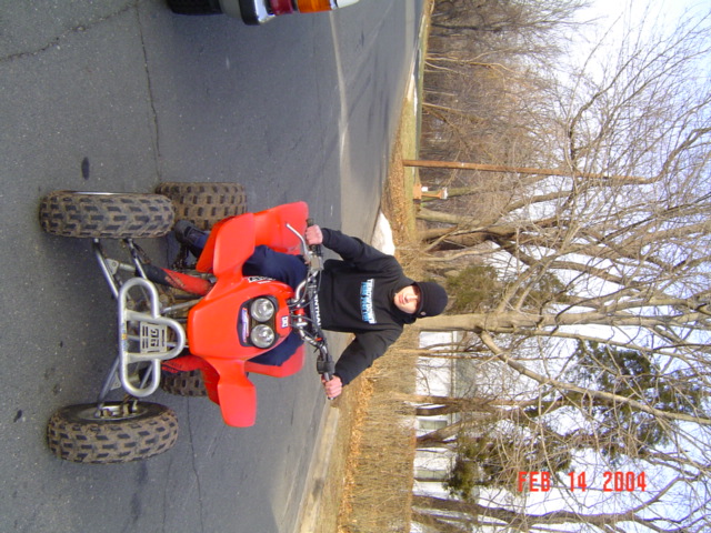 guy on red quad bike, wearing black hoodie and beanie, outside on a paved road