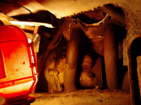1973 Ford F-250 - A close-up view of the underside of a vehicle, showing rusty metal components and a red work light illuminating the area.