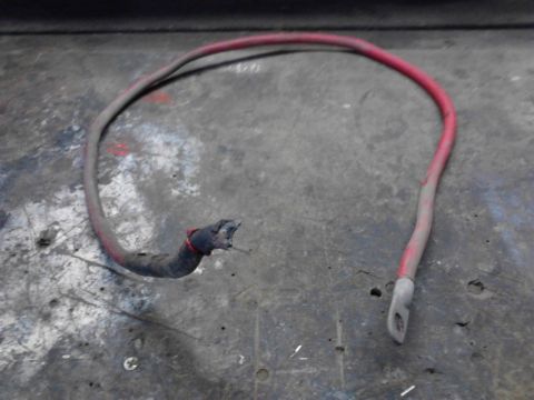1973 Ford F-250 - A red and gray battery cable with a damaged end is lying on a textured gray surface. One end of the cable has a metal eyelet, while the oth…