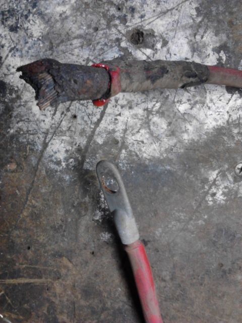1973 Ford F-250 - A damaged red battery cable with a frayed end is shown on a dirty, textured surface. Another red cable with a metal terminal is in the fore…