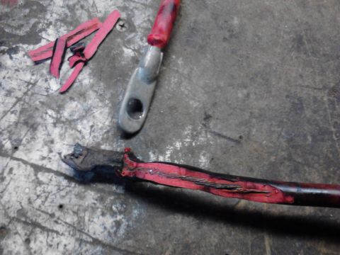 1973 Ford F-250 - Two damaged red battery cables with metal terminals are shown on a textured surface. One cable is severed, exposing frayed wires, while the…