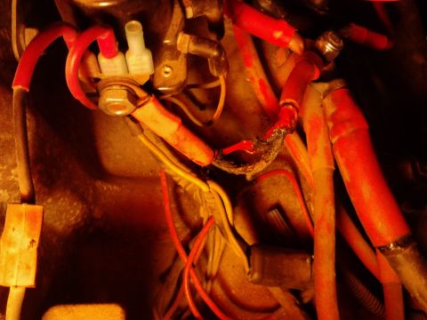 1973 Ford F-250 - Close-up view of frayed and burnt red electrical wiring connected to a terminal block on a vehicle. The damaged wires appear to be part of…