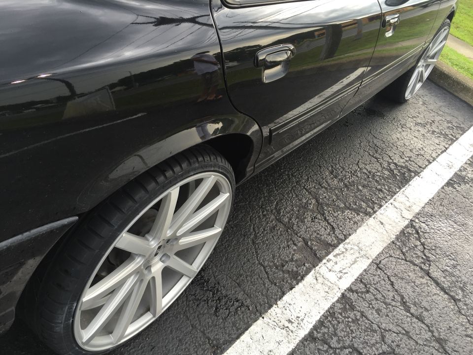 Black sedan side view with custom silver wheels parked on asphalt.