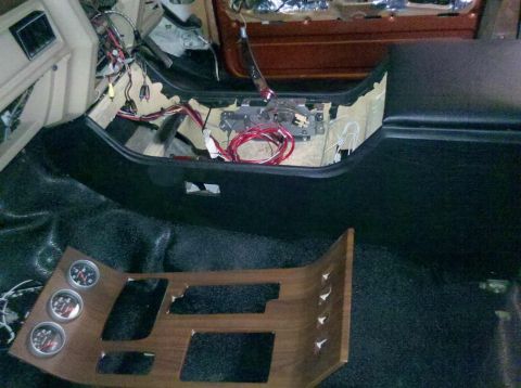 1982 Ford Bronco - The interior of a vehicle undergoing modification shows the center console area with exposed wiring and a removed wood-grain trim piece wit…