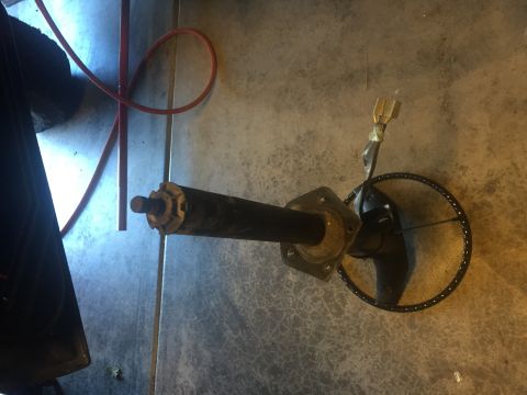1978 Ford Bronco - A steering column with a steering wheel attached is lying on a concrete floor. A red hose is visible in the background.