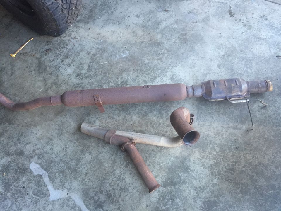 Rusty exhaust system parts including a catalytic converter and muffler on concrete.