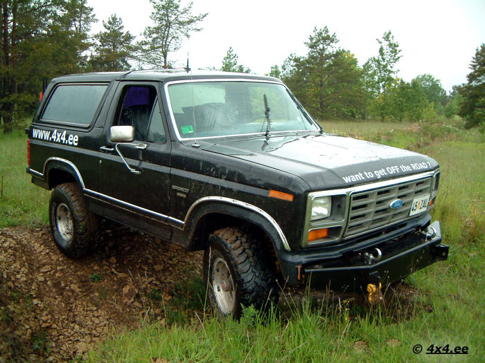 Black 1980s Ford Bronco with 4x4.ee decals and winch bumper on a muddy forest trail