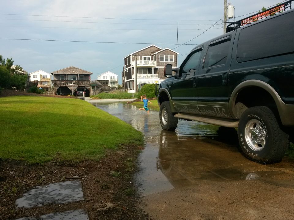 Dark green Ford Excursion parked in shallow water with a boy running in the background.
