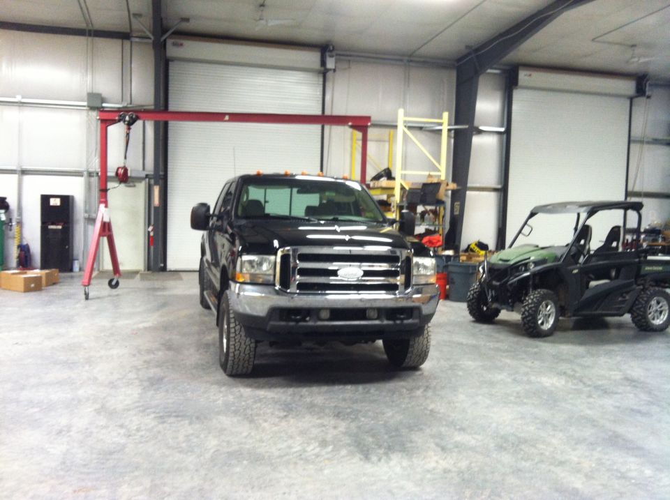 Black Ford F-250 pickup truck in a garage with a UTV and gantry crane.