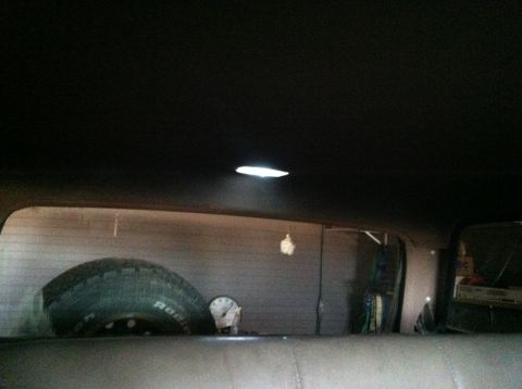 2004 Ford F-250 - Interior view of a vehicle showing a spare tire mounted vertically behind the rear seats, with a clock visible to its right. A dome light i…