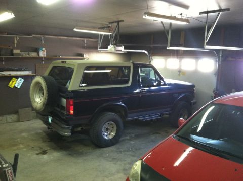 2004 Ford F-250 - A dark blue Ford Bronco with a tan top is parked inside a garage. The vehicle has a spare tire mounted on the rear door and is seen from th…