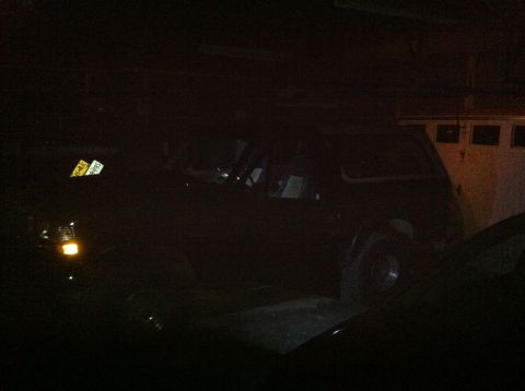 2004 Ford F-250 - A dark-colored SUV is parked in a garage with its headlights on. A yellow license plate with black text is visible on the front of the vehi…