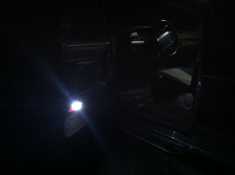 2004 Ford F-250 - The interior of a dark vehicle is illuminated by a bright LED light mounted on the driver's side door panel. The steering wheel and dashboa…